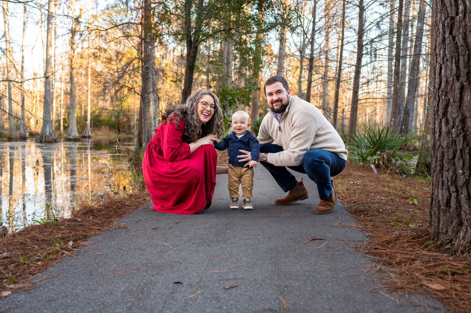 Nikki and Trent crouch down on a path at Cypress gardens with their toddler son