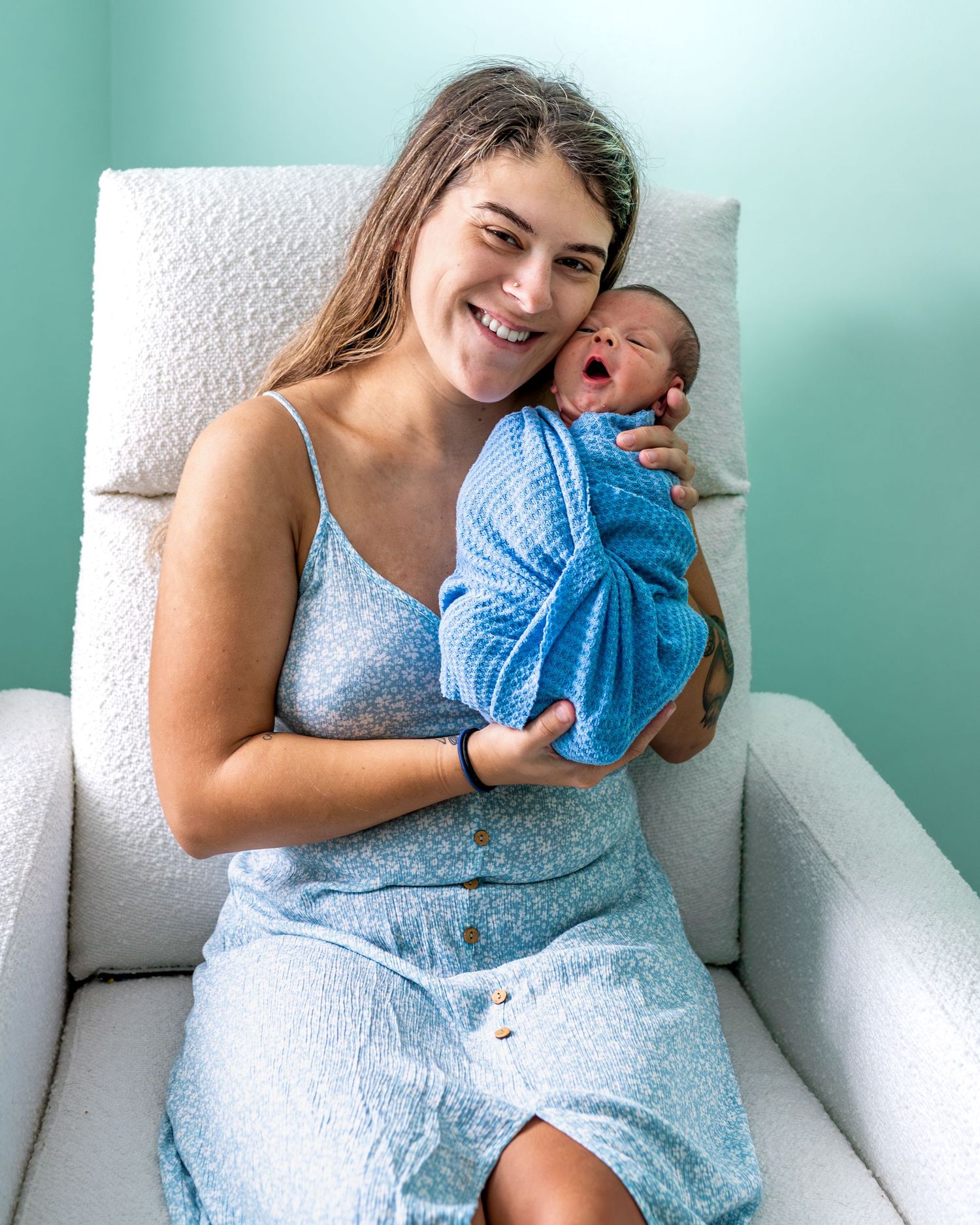 A tender moment with a newborn baby wearing a blue outfit in a cozy armchair.
