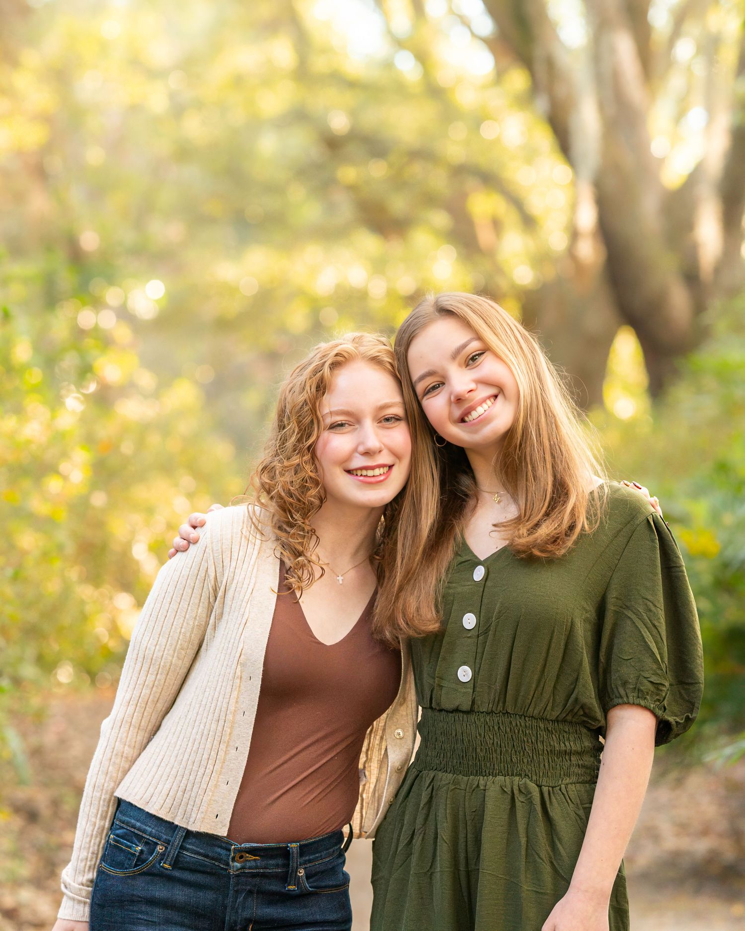 Two people share laughter while posing against an autumn backdrop with golden sunlight filtering through trees.