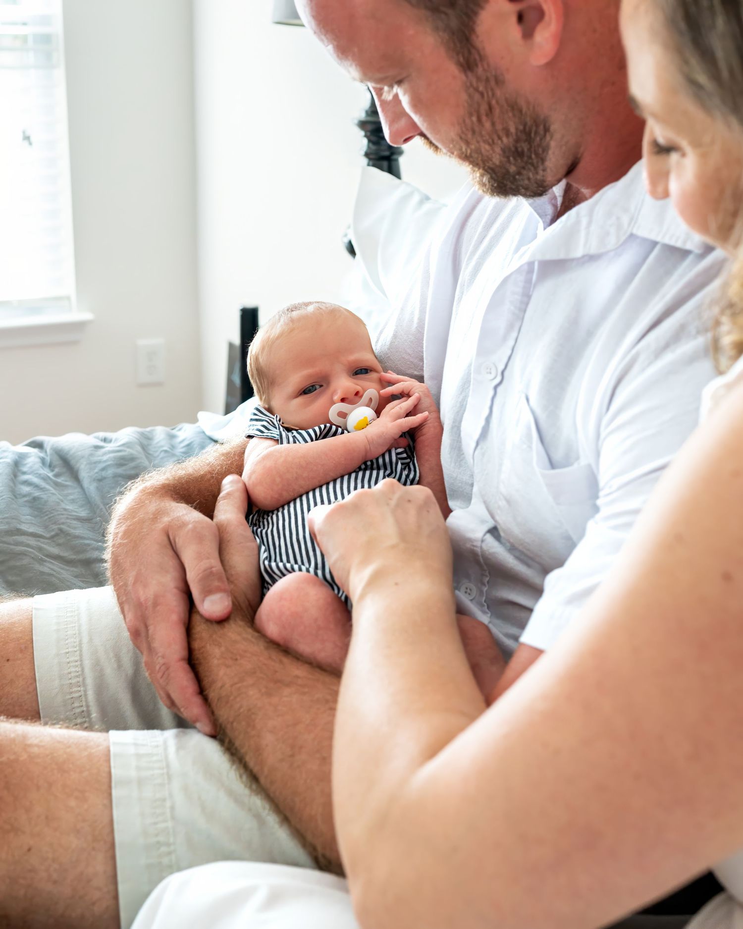 Close up of a newborn little boy being held in his father's arms as his mother interacts with him