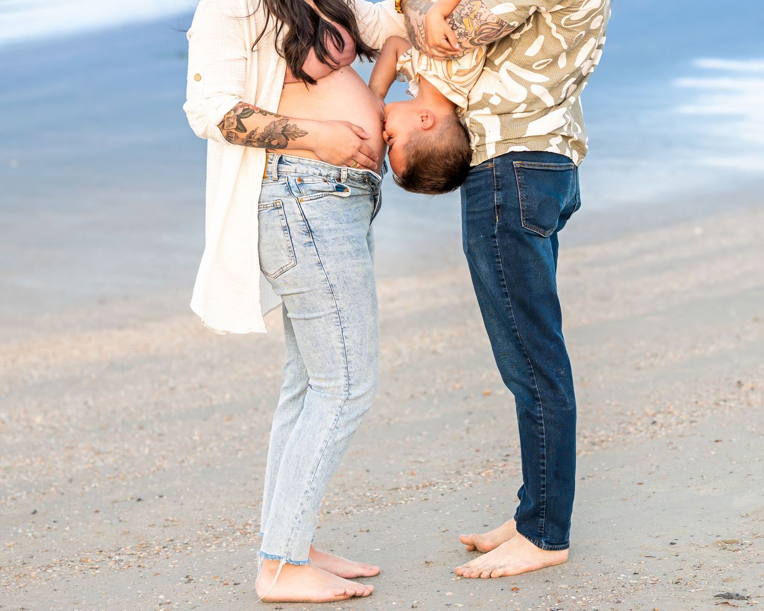 Dad holds his toddler upside down so that he can kiss his mom's pregnant belly.