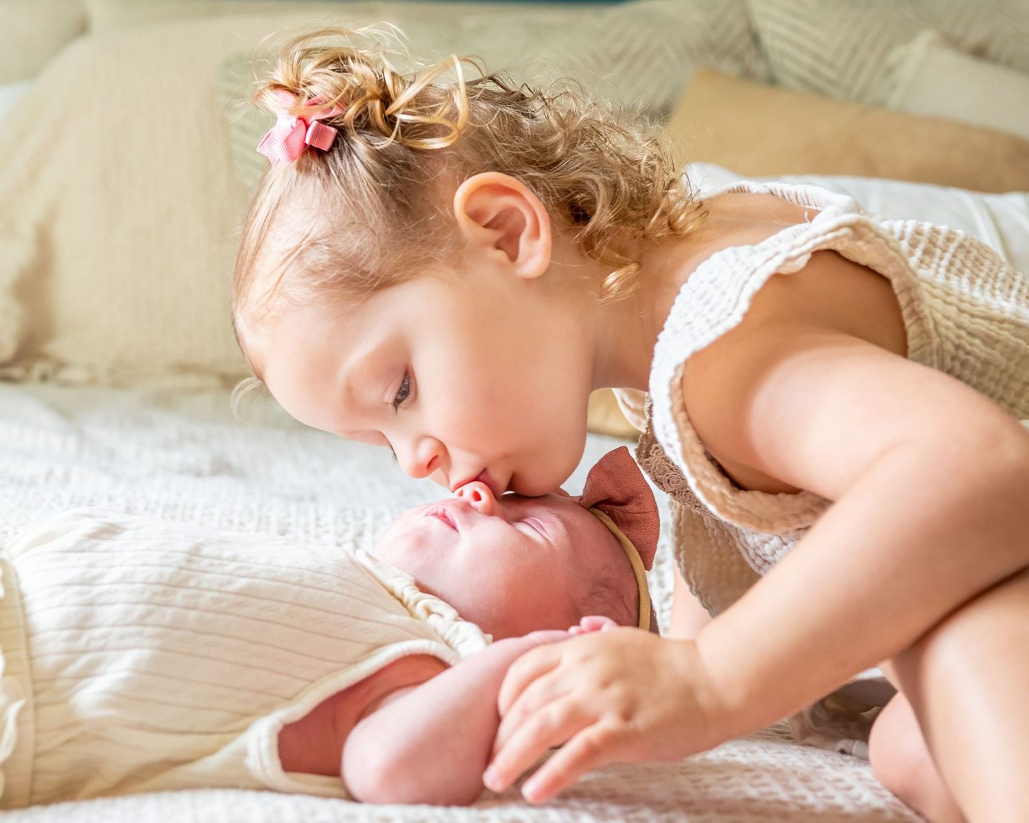 Toddler lying on bed looking at small baby with gentle expression.