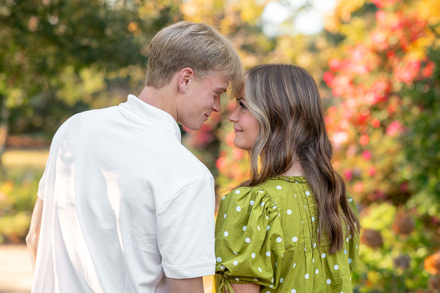 Couple embraces in a romantic outdoor setting with vibrant fall foliage creating a warm autumn backdrop.