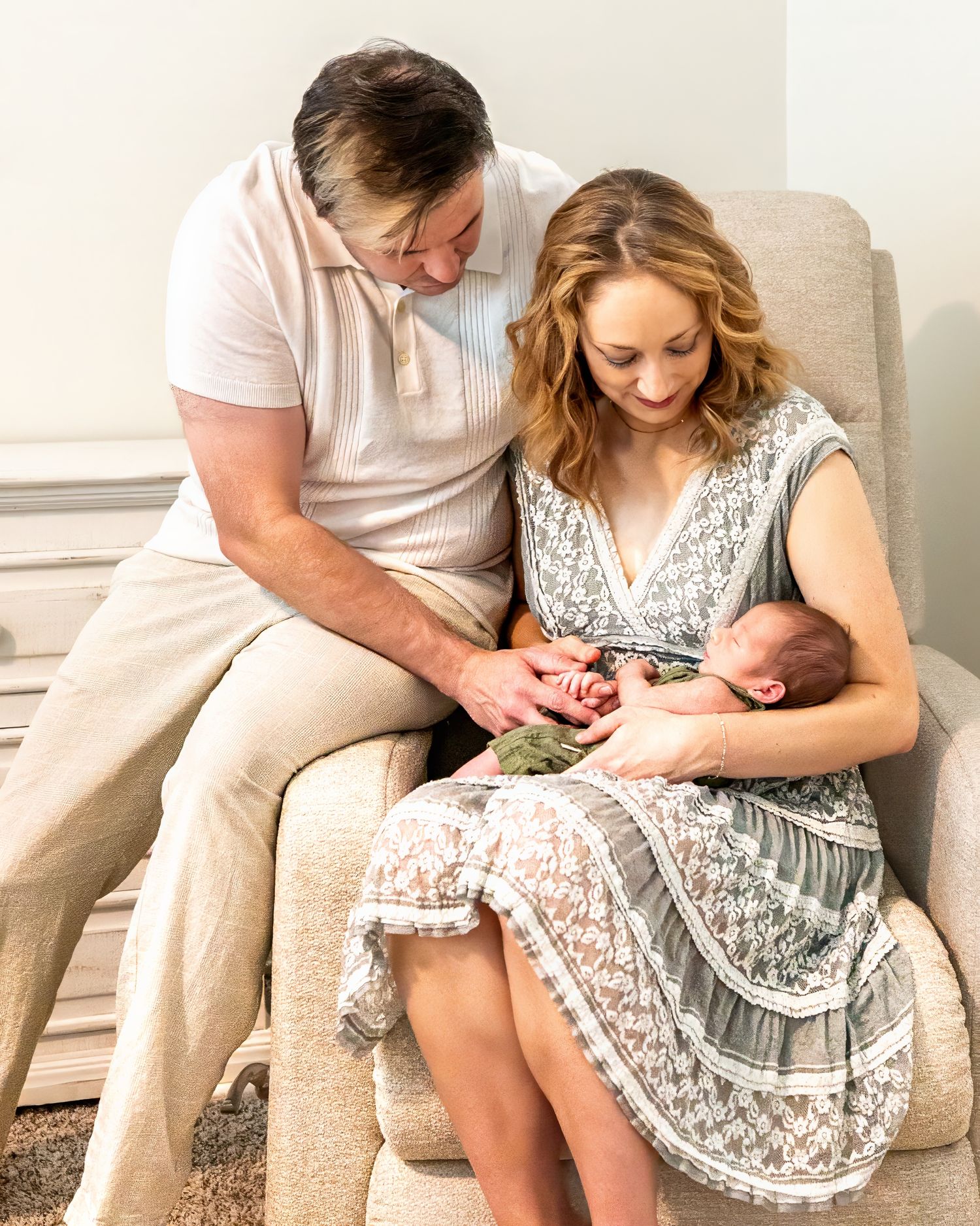 A young family tenderly gathers on a rocker sharing a precious moment with their newborn baby at home.