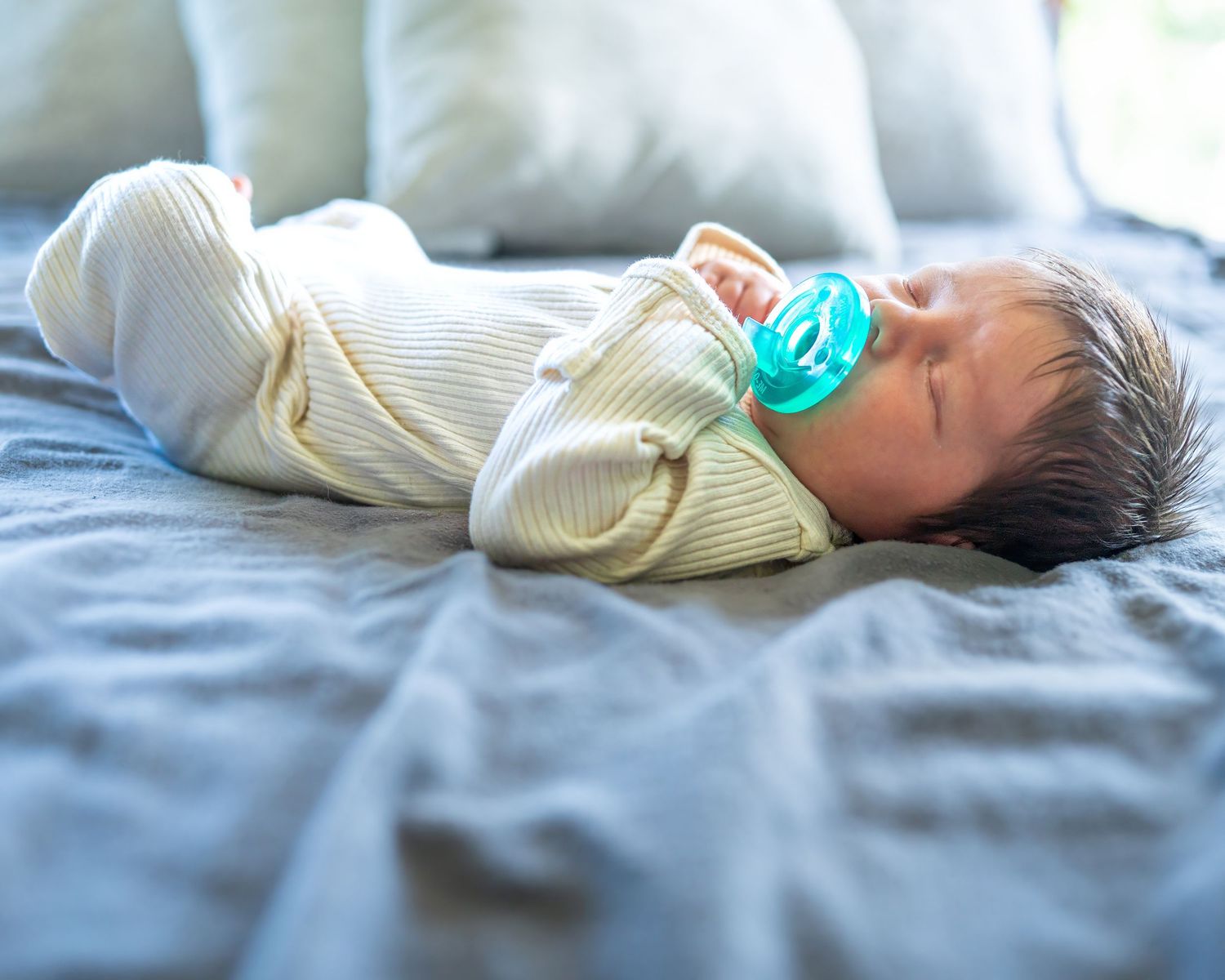 Infant sleeping peacefully on white bedding in soft natural light.