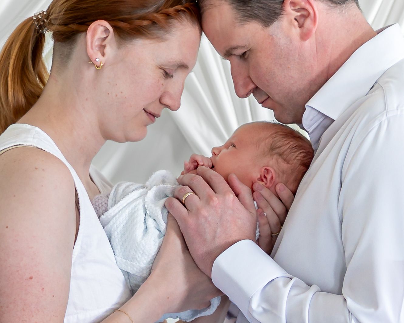 New parents tenderly holding their newborn baby together, sharing a precious bonding moment in soft white light.