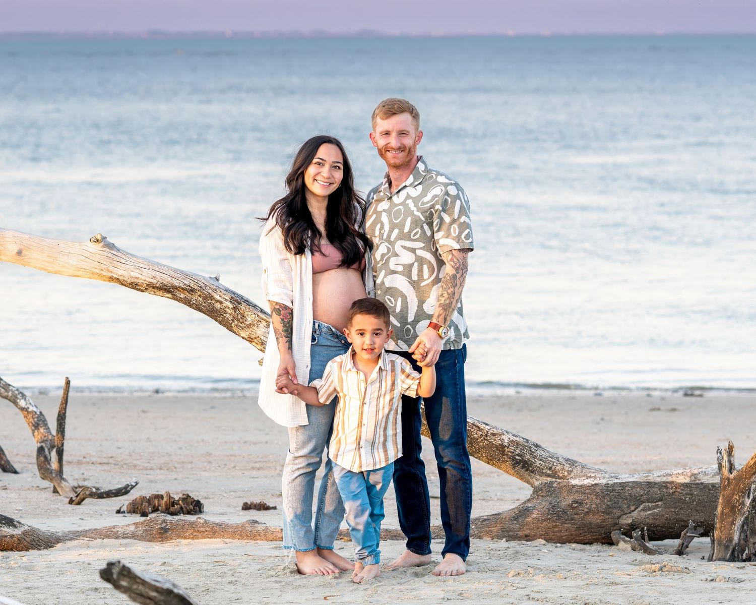 A family stands together on a beach at sunset with driftwood and ocean waves in the background.