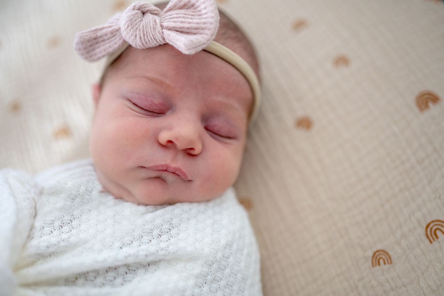 Close up of newborn little girl with light pink headband, sleeping in her crib