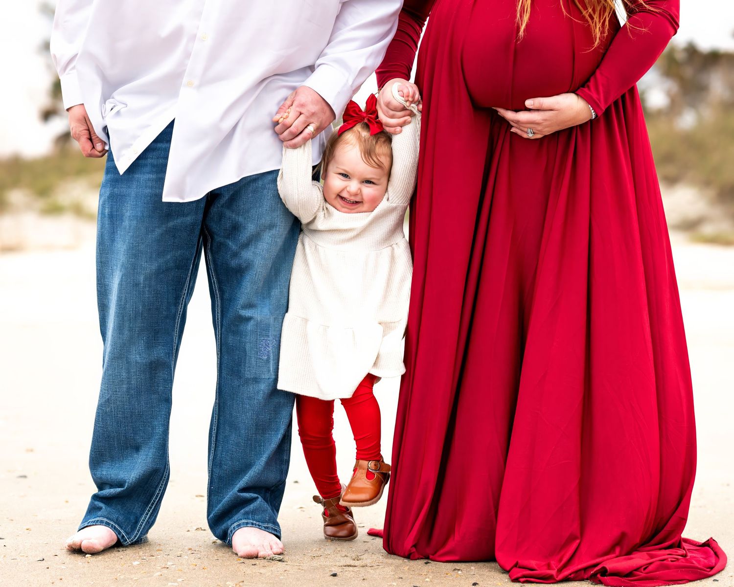 A row of people wearing red and white outfits stand together on the while holding hands. Photo emphasizes the toddler and mom's pregnancy.