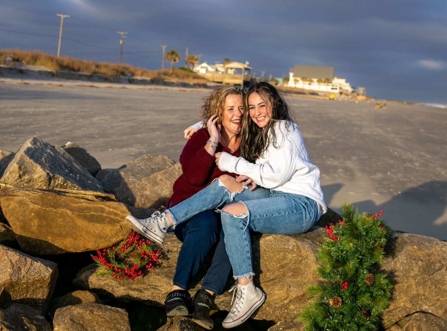 Angel and her teenage daughter embrace and laugh on the rocks at the beach on Folly