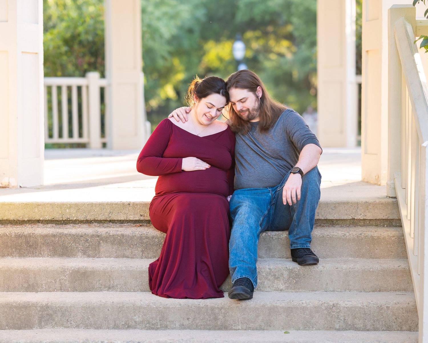 Couple sitting on porch steps sharing intimate moment during maternity photo session.