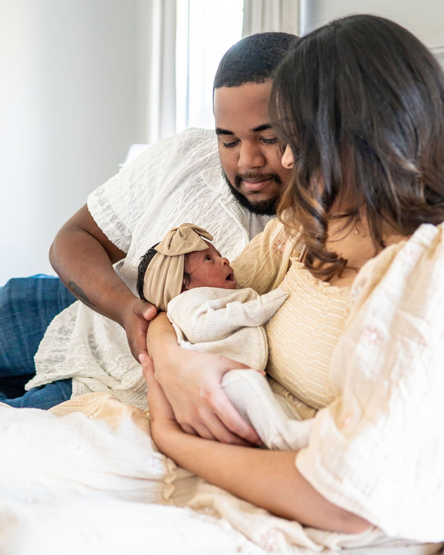Intimate family moment captured in bright indoor setting with white bedding.