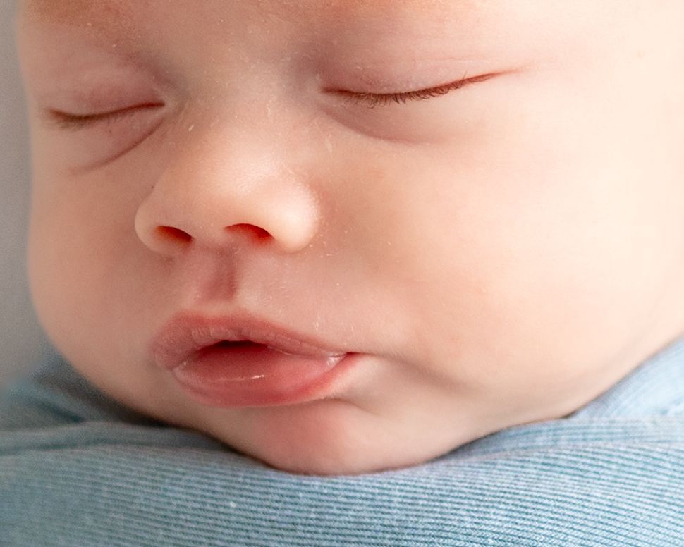 Close-up of a sleeping newborn baby with delicate features, soft skin, and tiny lips, wrapped in a light blue blanket.