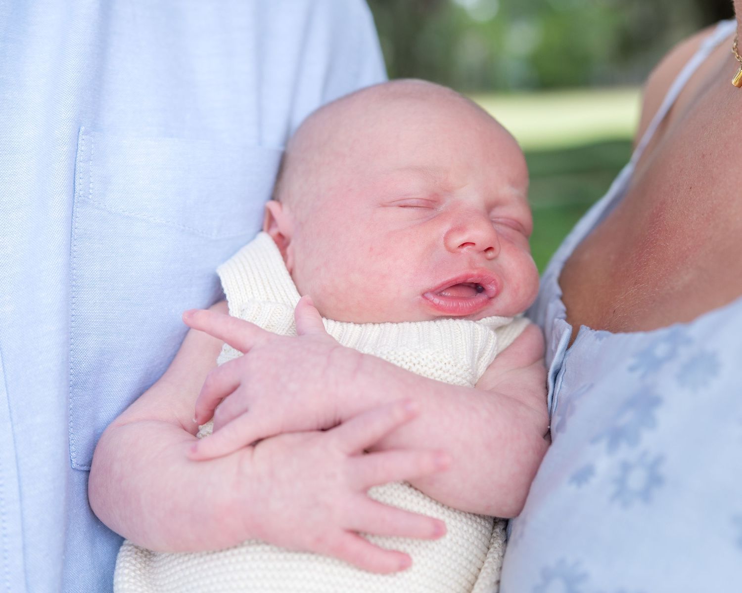 Close up of newborn baby boy sleeping in the arms of his mom and dad as they stand side by side
