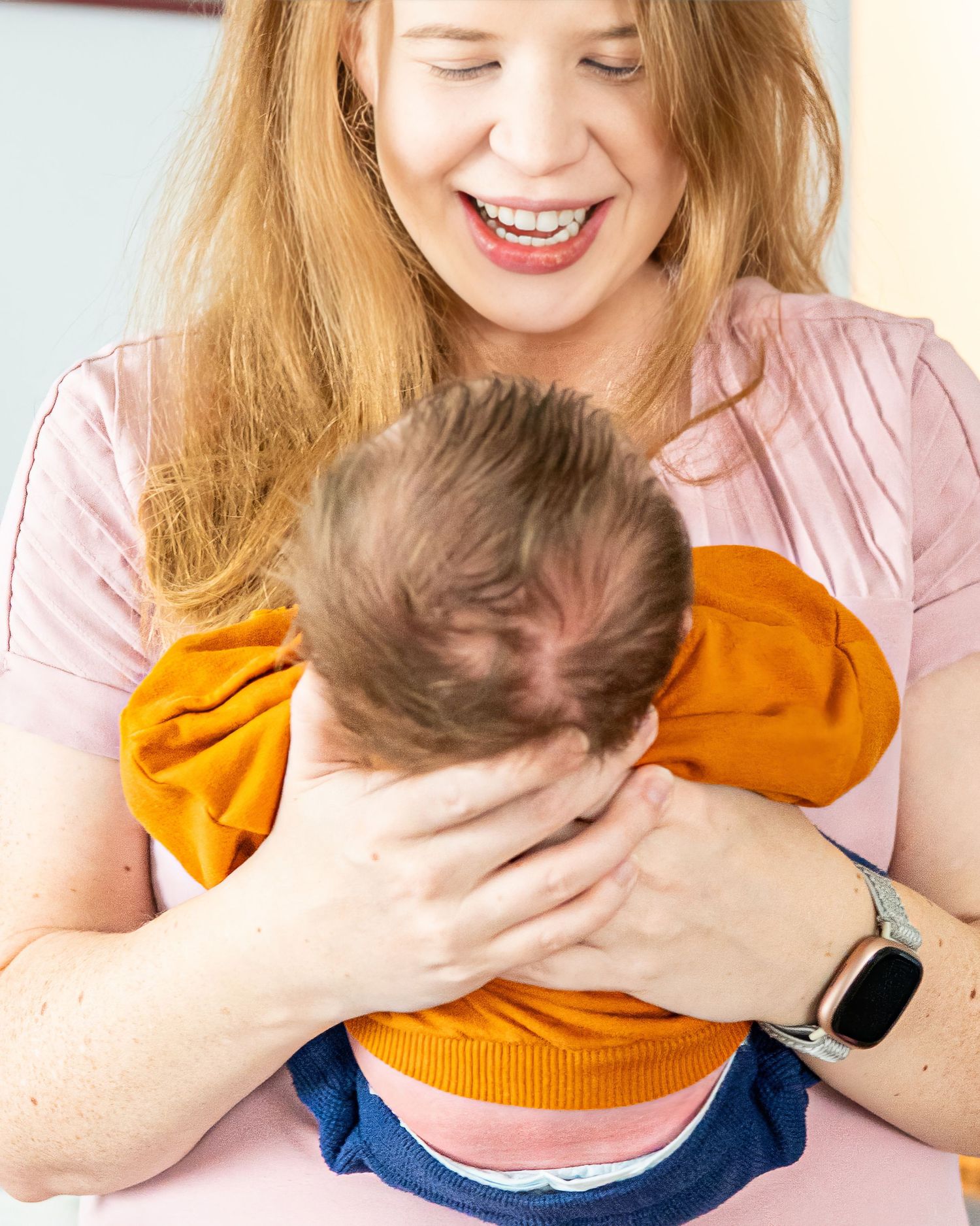 A mom holds her newborn and smiles down at him. we see his head of hair and her big smile.