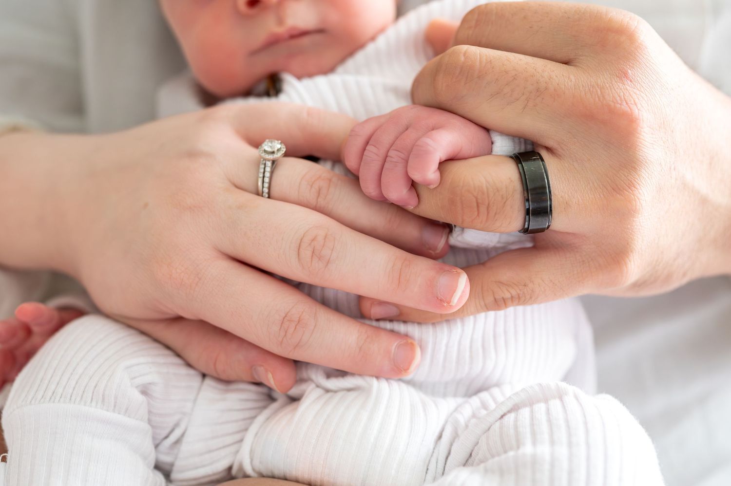 Close-up details of hands holding newborn in white clothing.