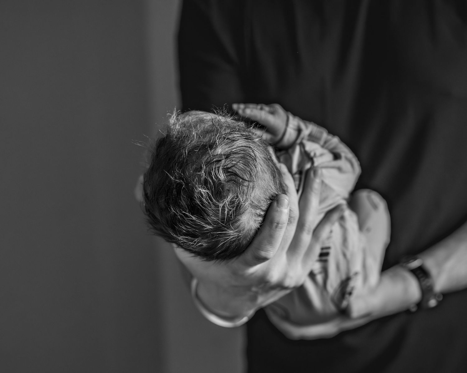 Close up photo of a father holding his newborn - featuring dark swirls in newborn's hair. photo is in black and white