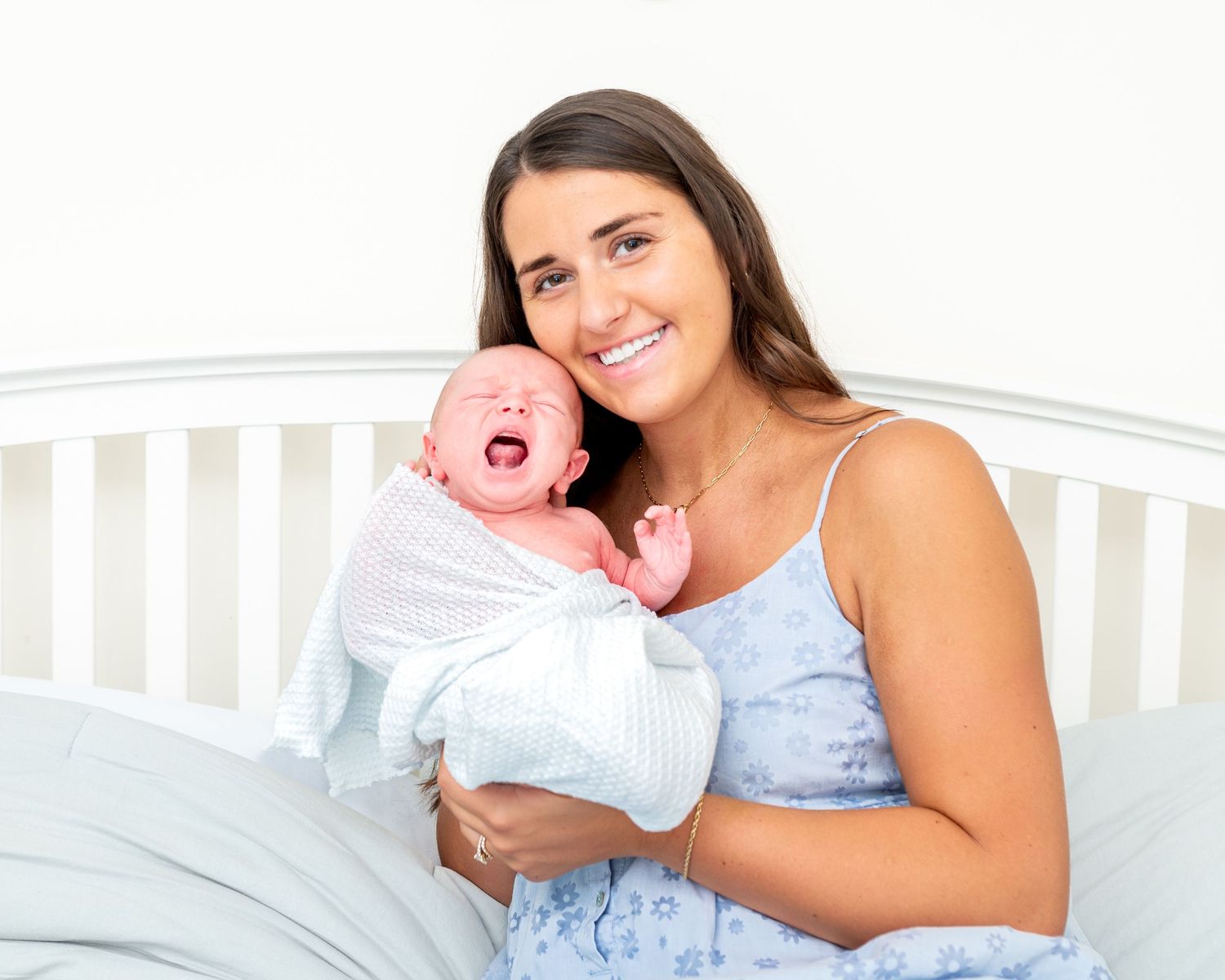 Mom holds her newborn son so that they are cheek to cheek, newborn is crying