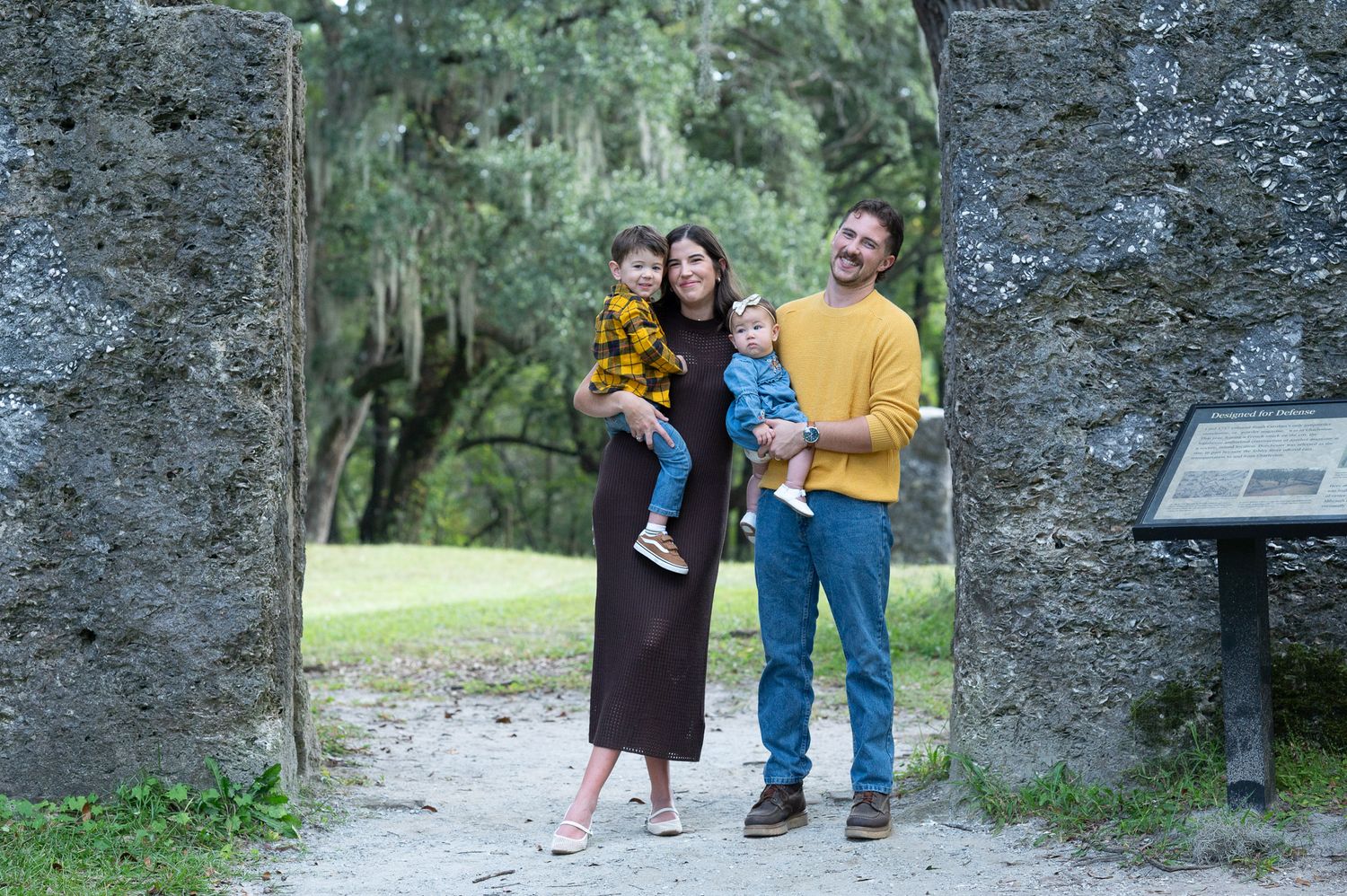 Unedited photo: A family stands next to a rocky wall in wearing coordinating fall colors in yellows and browns