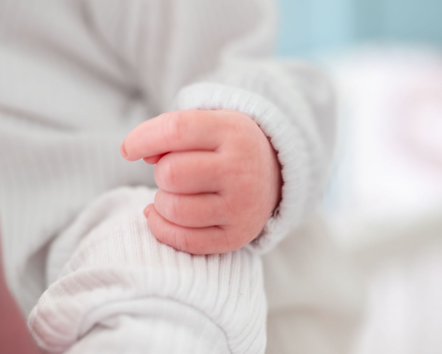 Detail shots of tiny newborn hands and white clothing.