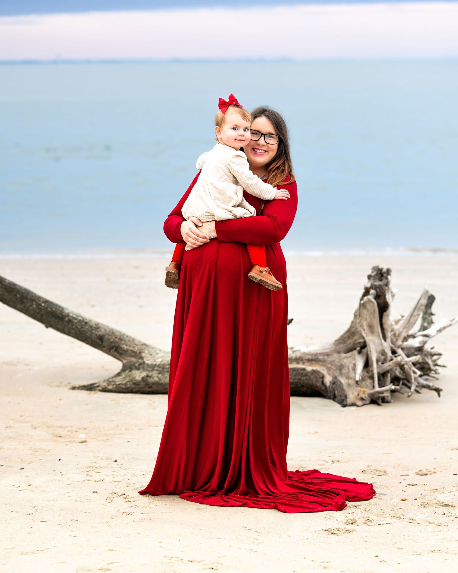 A beach portrait featuring flowing red gowns against a serene coastal backdrop with driftwood on the sand.
