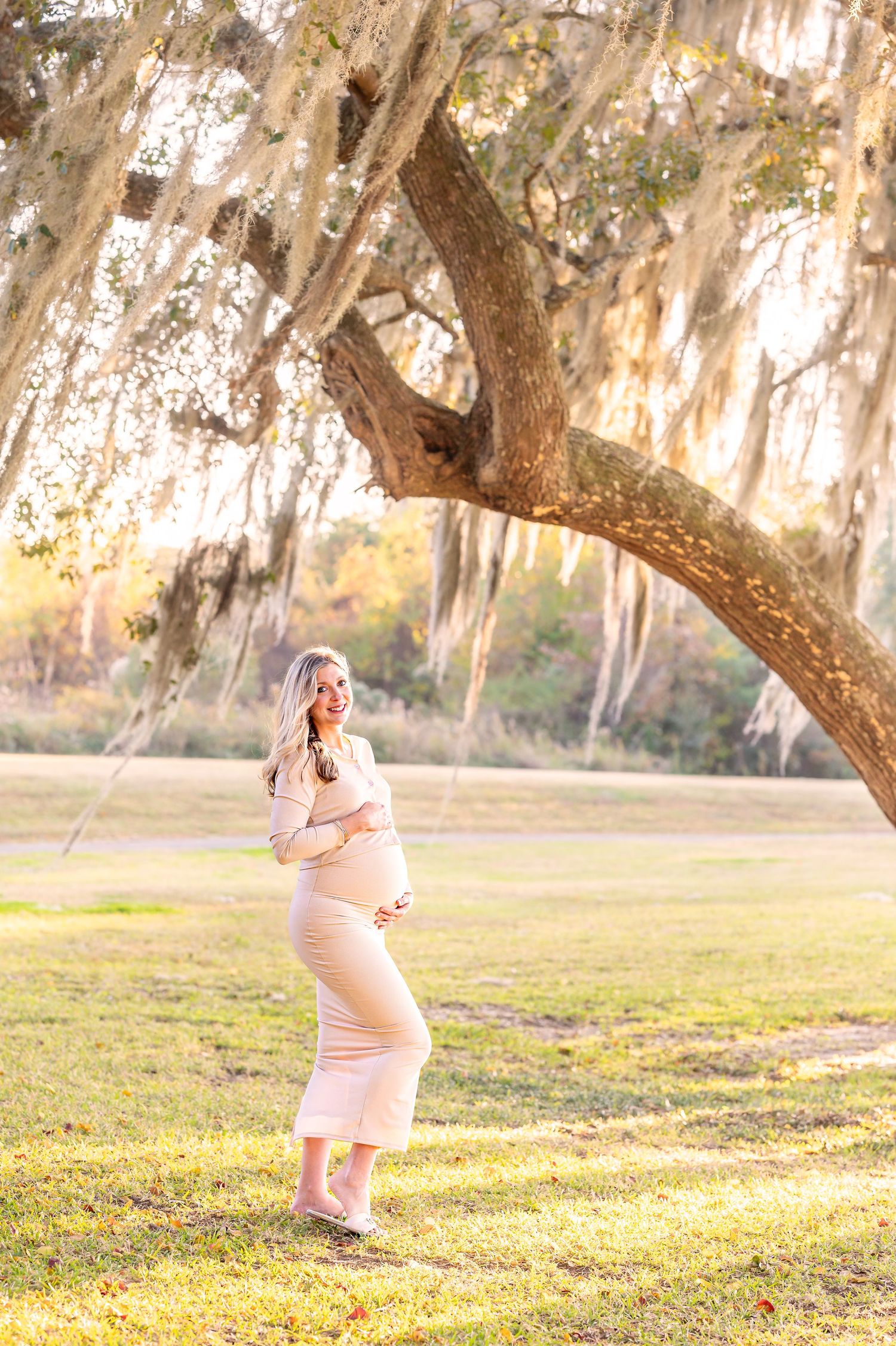Maternity photos in a dreamy outdoor setting with Spanish moss and golden sunlight.