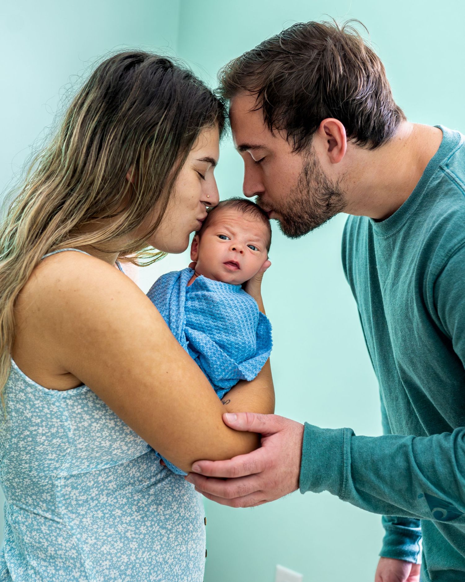 An intimate family portrait sharing a tender moment with their newborn in a blue outfit.