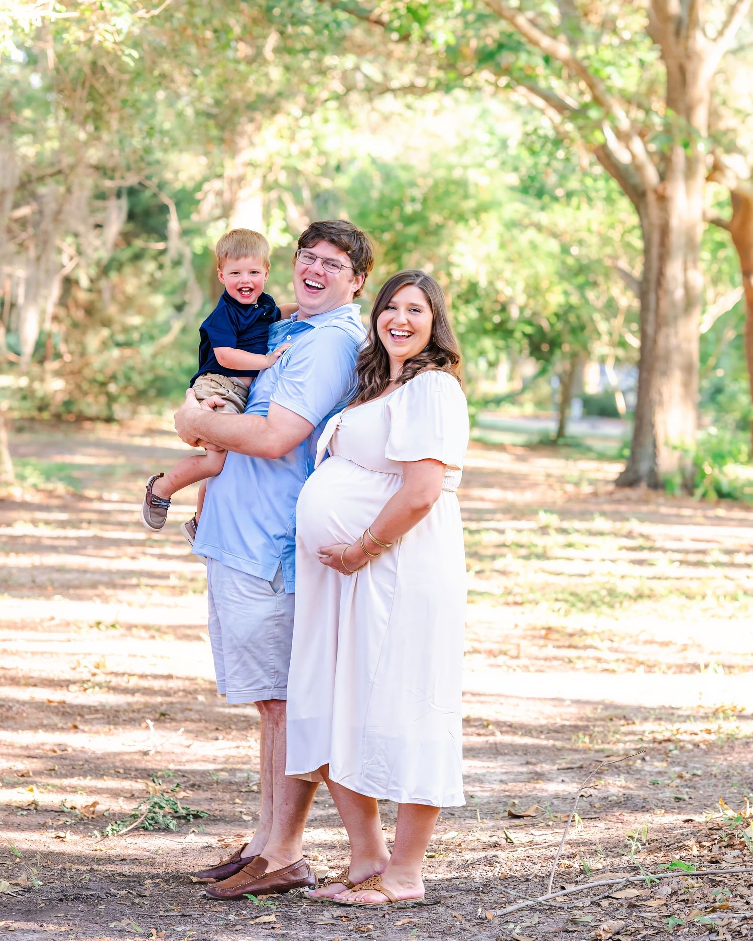 Mom and dad pose together while dad holds his toddler - all are looking at the camera smiling during their family maternity session