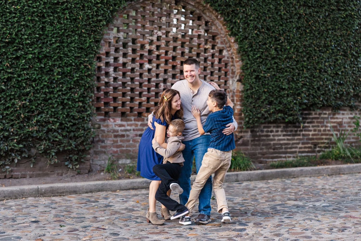 A series of candid outdoor family photo showing a couple and their two children, boys, against an ivy-covered brick wall.