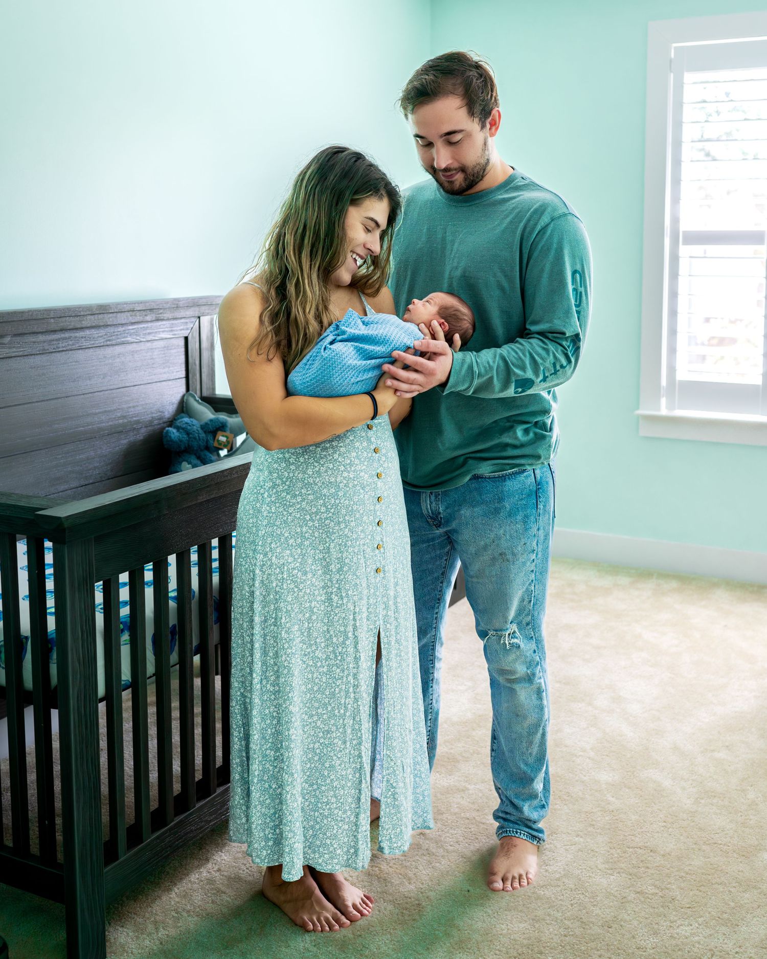 Parents standing together in mint green room with dark wood crib.