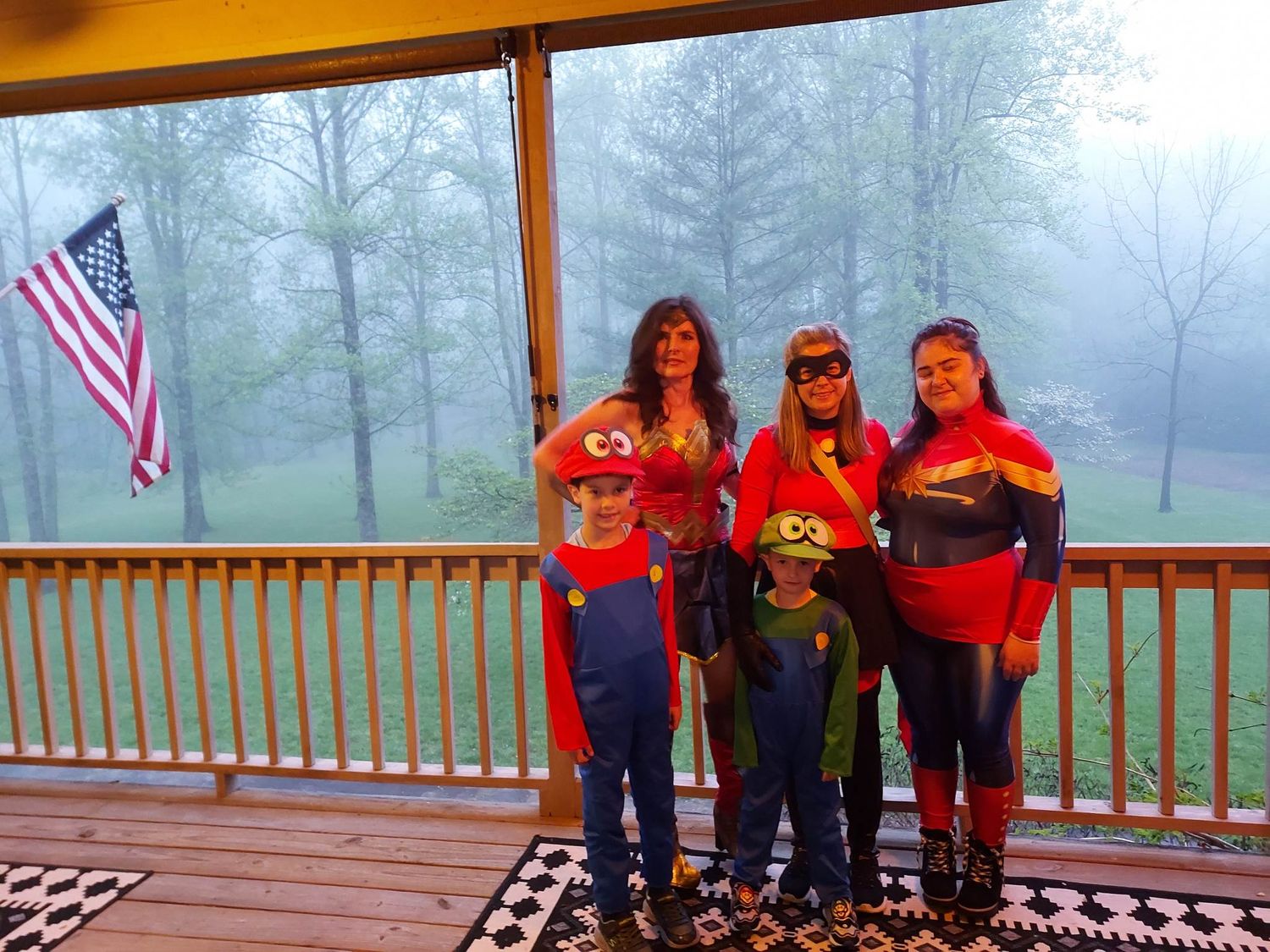 Three adults dressed in superhero costumes and two children dressed as Mario and Luigi pose for a photo