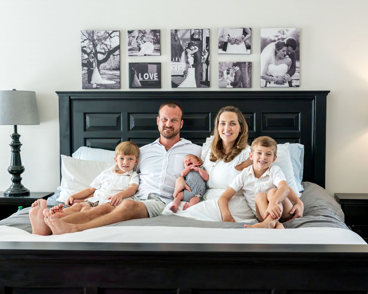 A relaxed family photo on a bed with black and white gallery wall photos above.