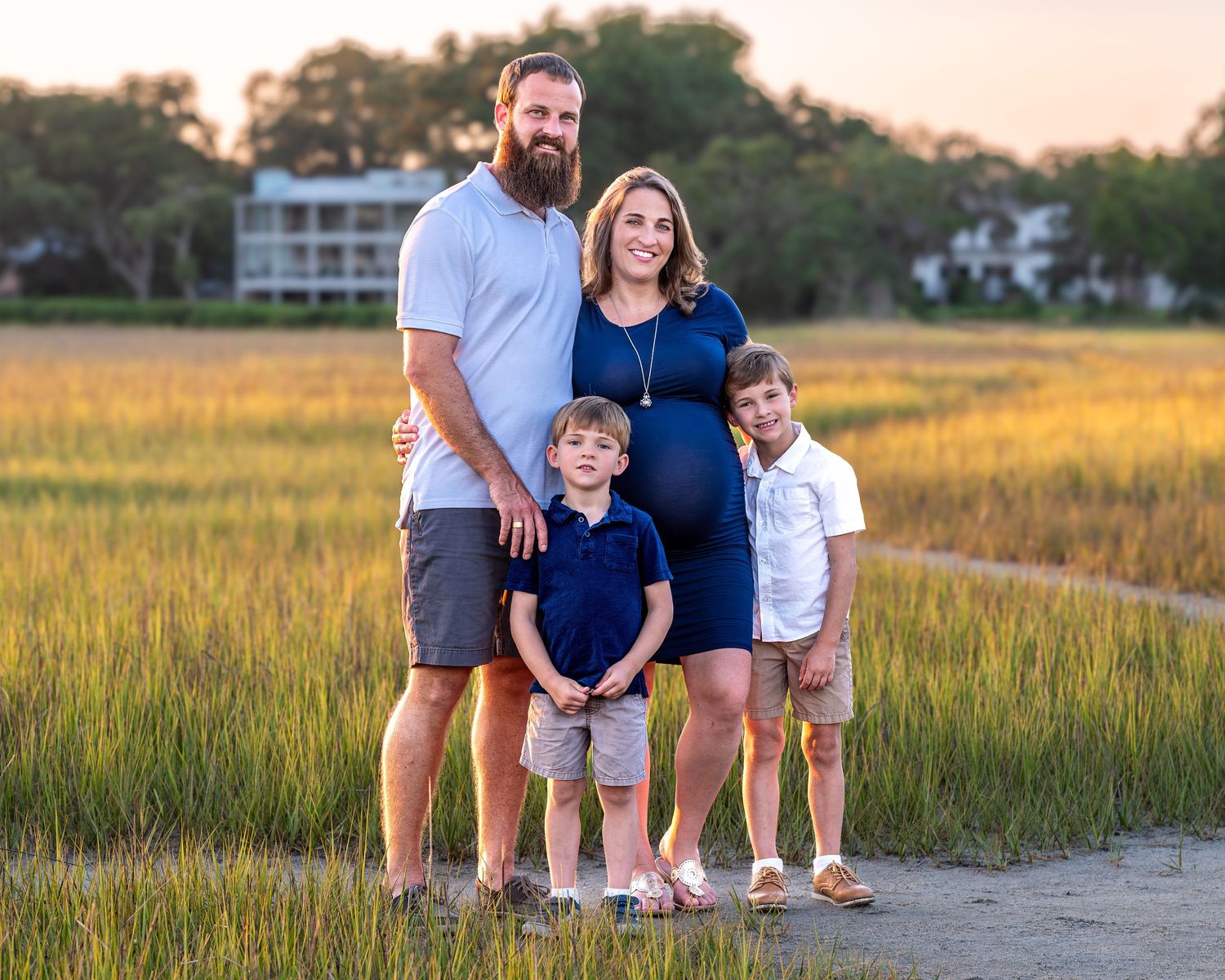 A family of four poses together in front of golden marsh grass at sunset.