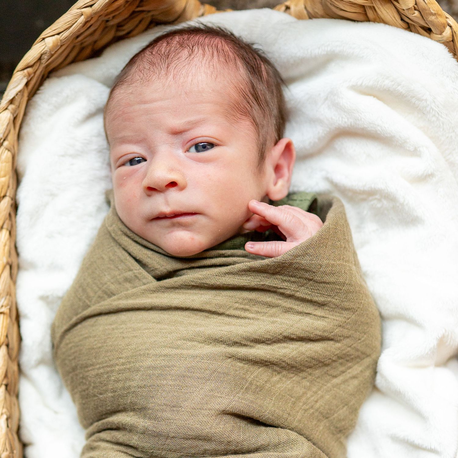 Newborn baby wrapped in olive green swaddle blanket on white bedding.