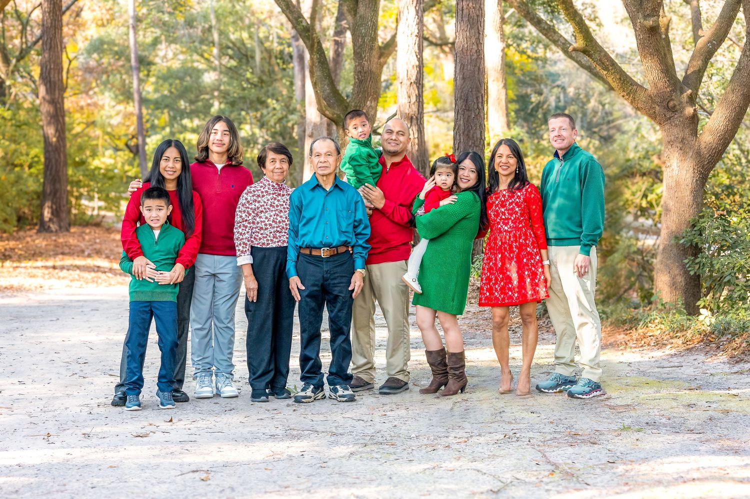Extended family in festive red and green attire poses together on wooded path at Azalea Park