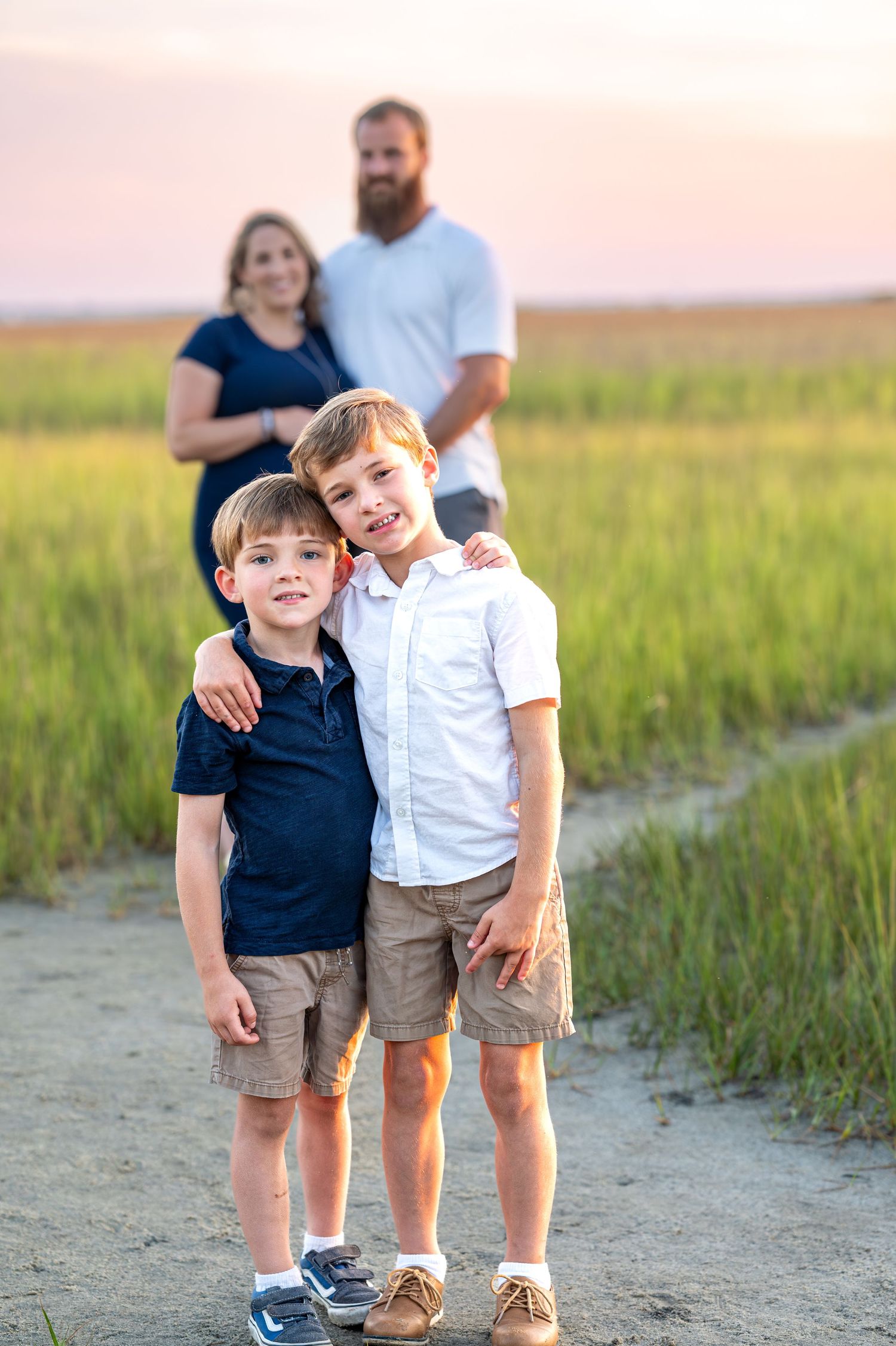 Two young boys pose on a dirt path with their parents standing behind them at sunset.
