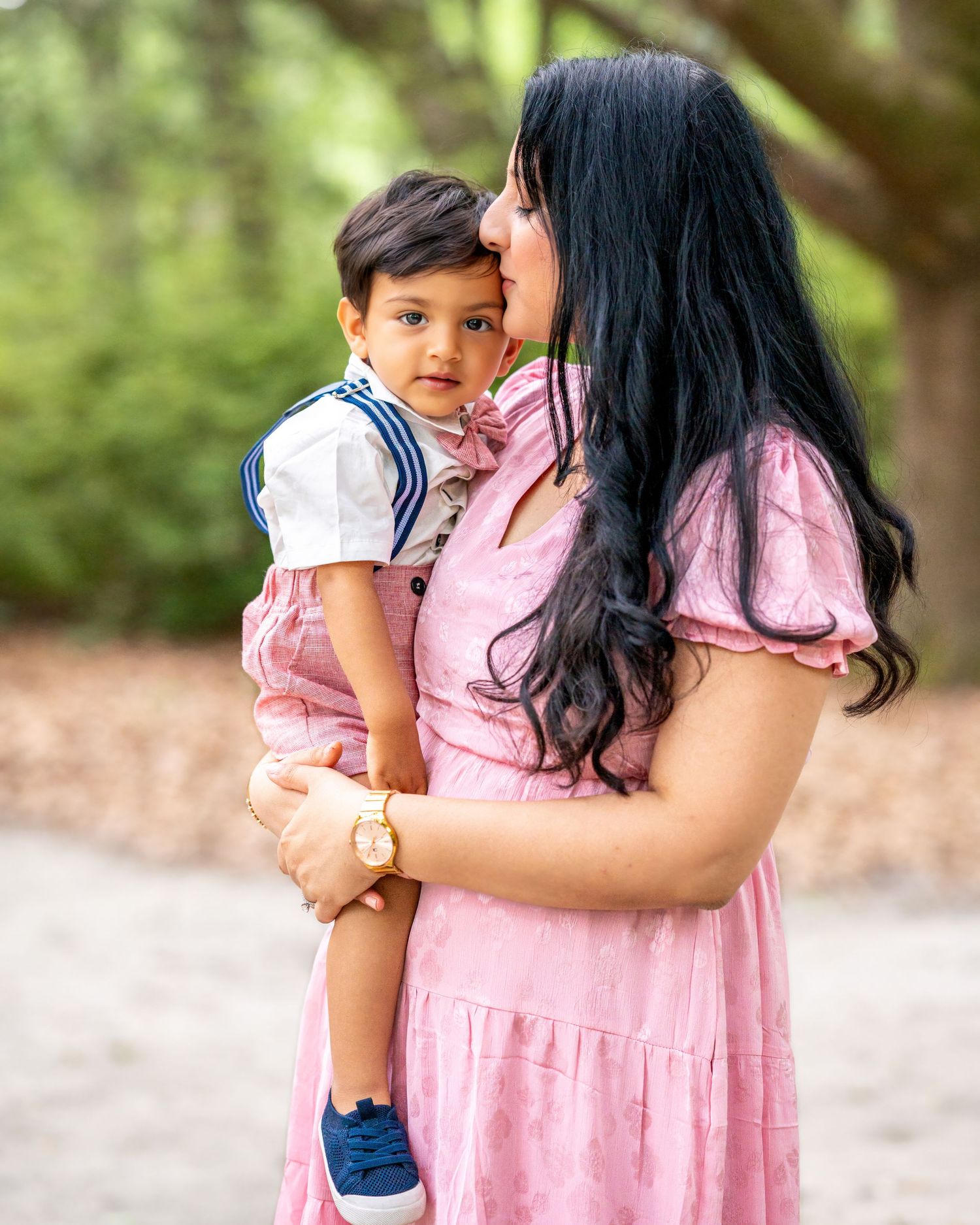 A small child in sailor-style outfit being held in a pink dress outdoors.