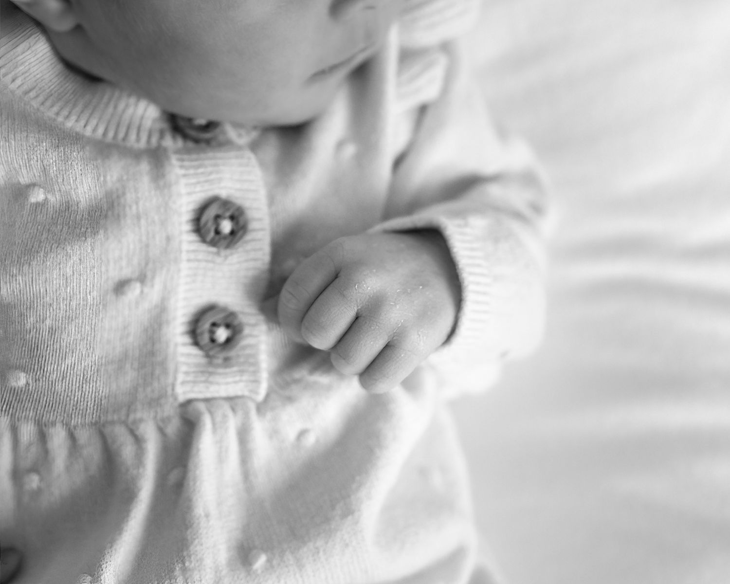 Close-up black and white image of an infant wearing a white knit sweater.