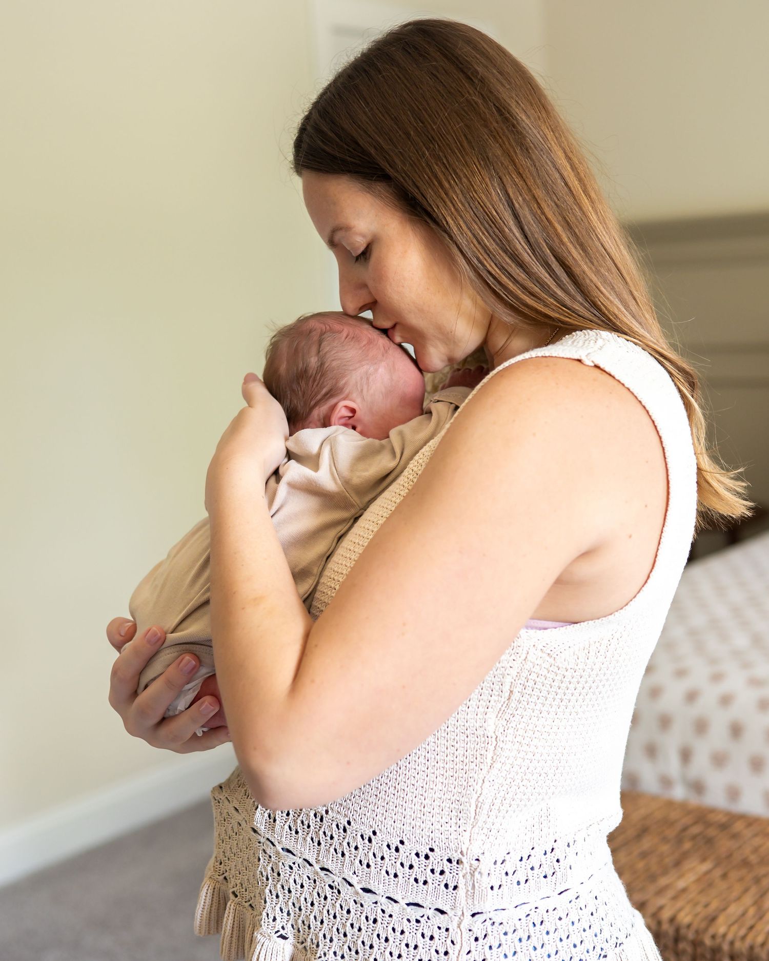 A mother tenderly kisses her newborn baby while cradling the infant close to her chest indoors.