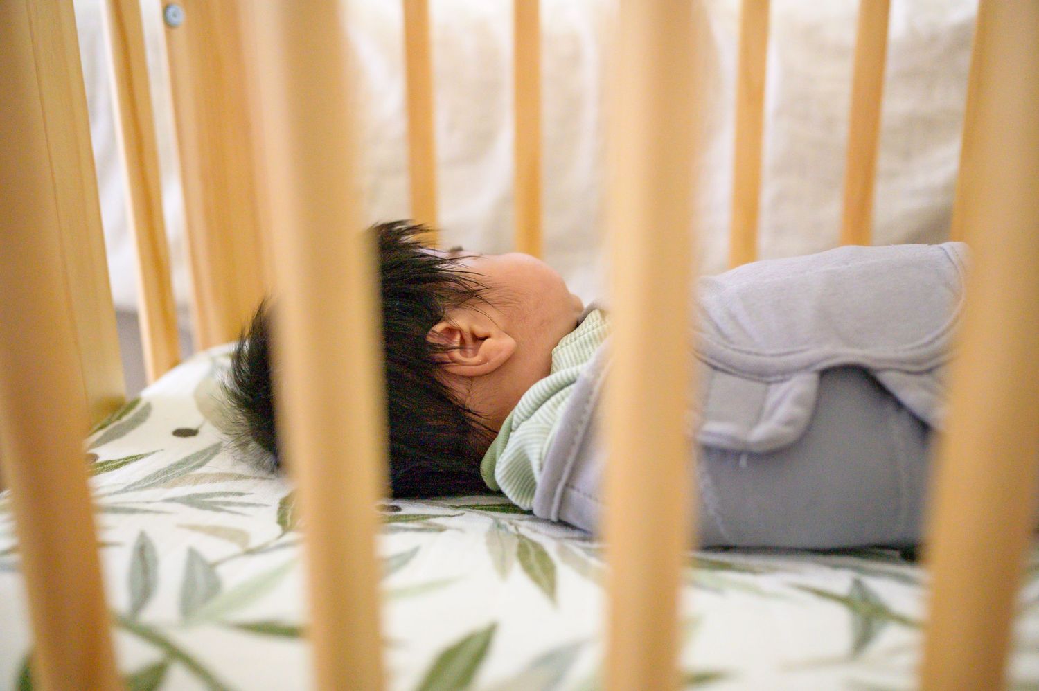 Newborn little boy with headful of black hair is swaddled and sleeping in crib