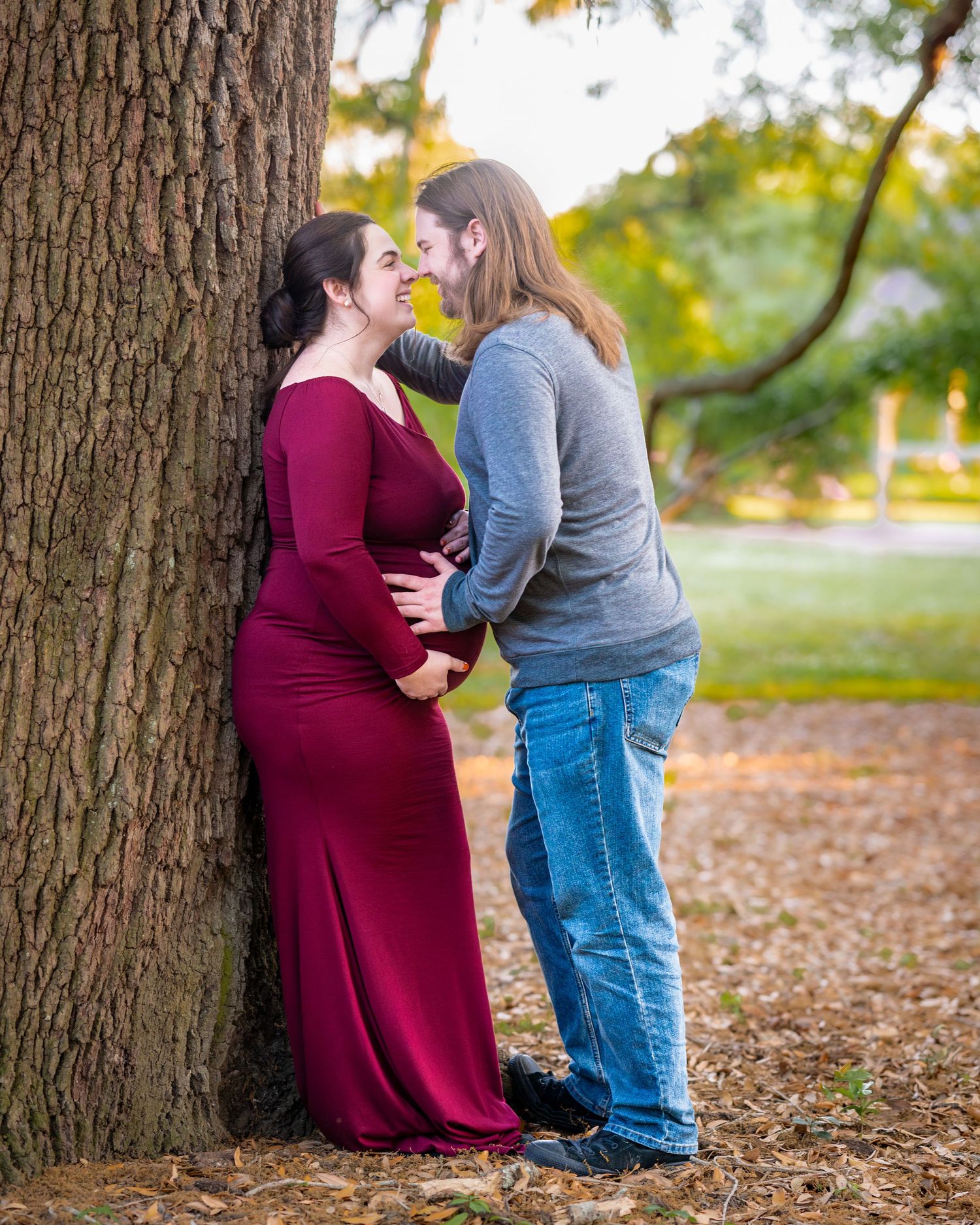 A romantic couple shares an intimate moment while standing beside a large tree trunk.