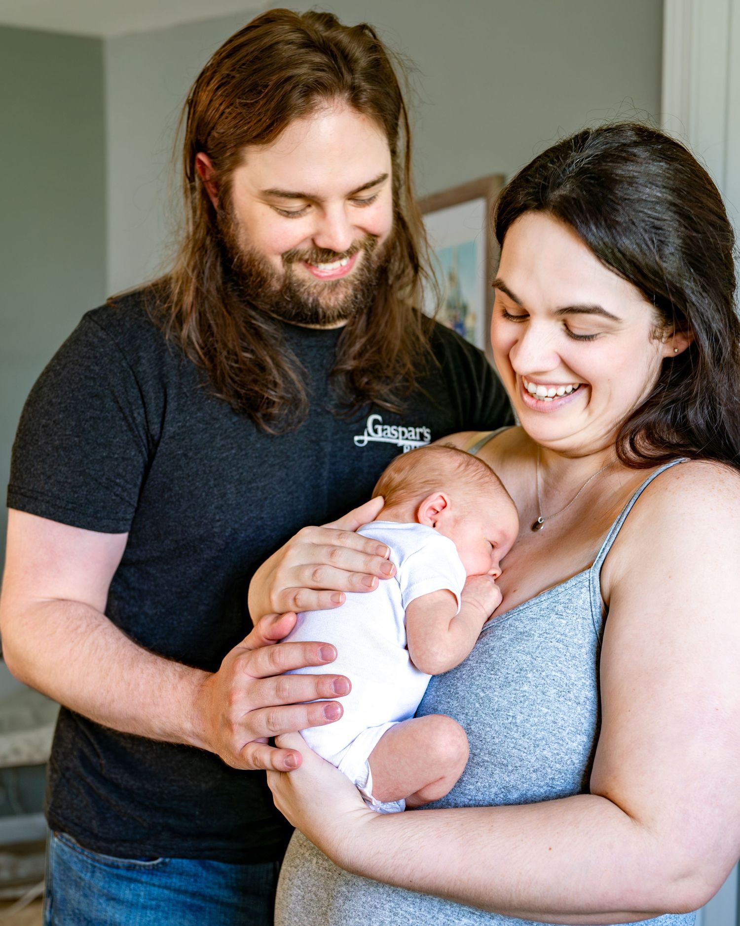 Parents share a tender moment with their newborn baby while posing together in a bright room.