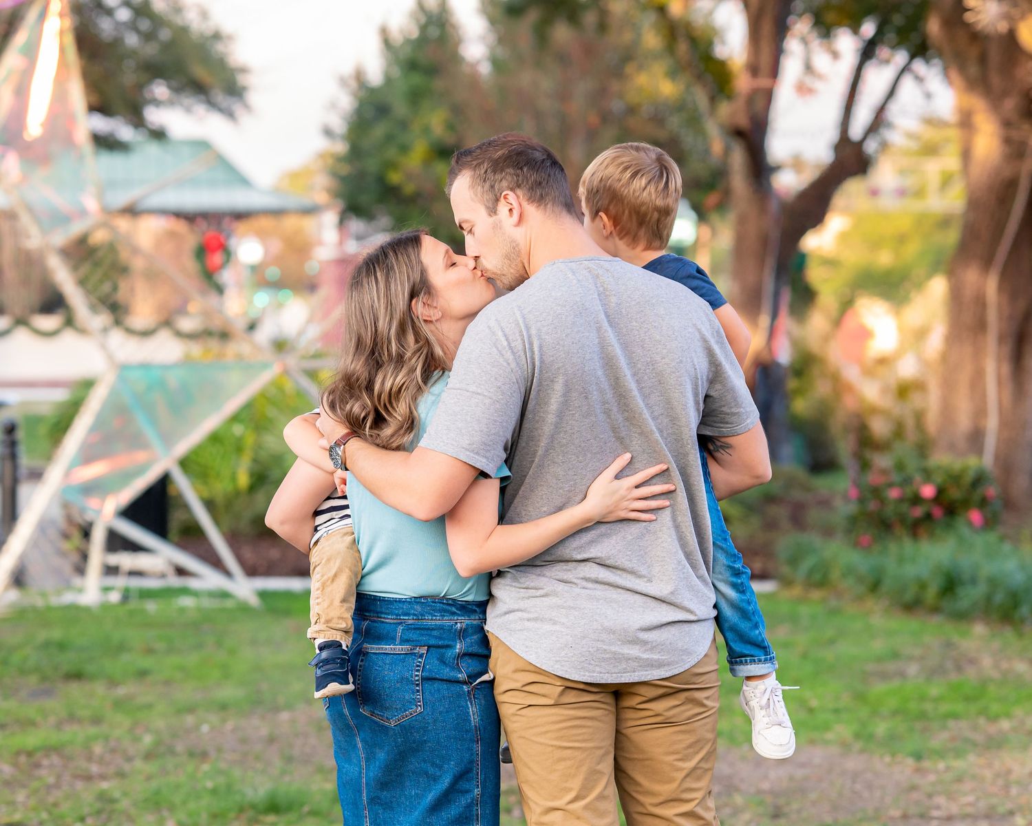 A couple embraces while walking along a grassy path during a casual outdoor photoshoot.