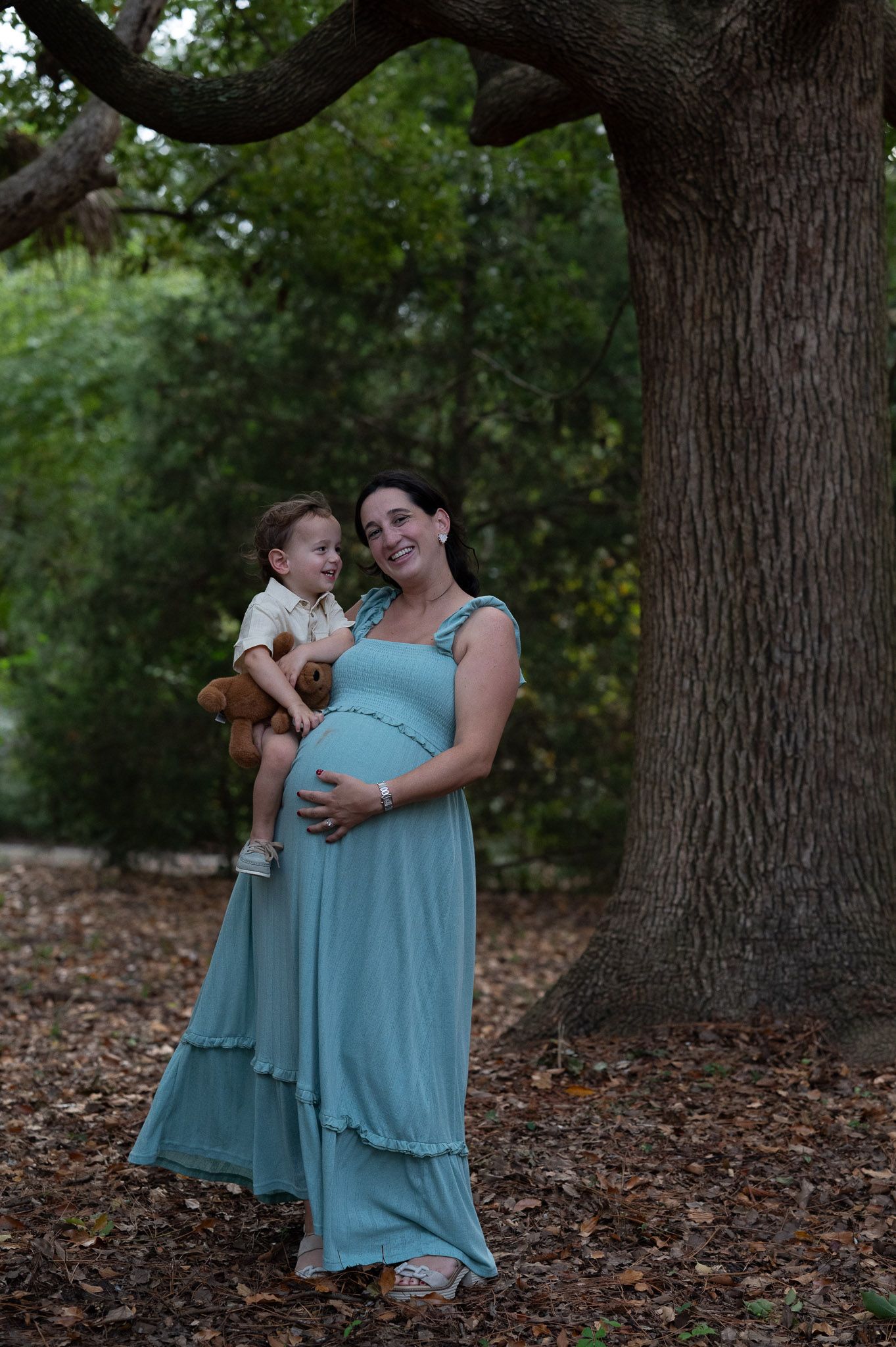 Maternity session, unedited photo, mom in blue dress holds her toddler son who is looking at her adoringly.