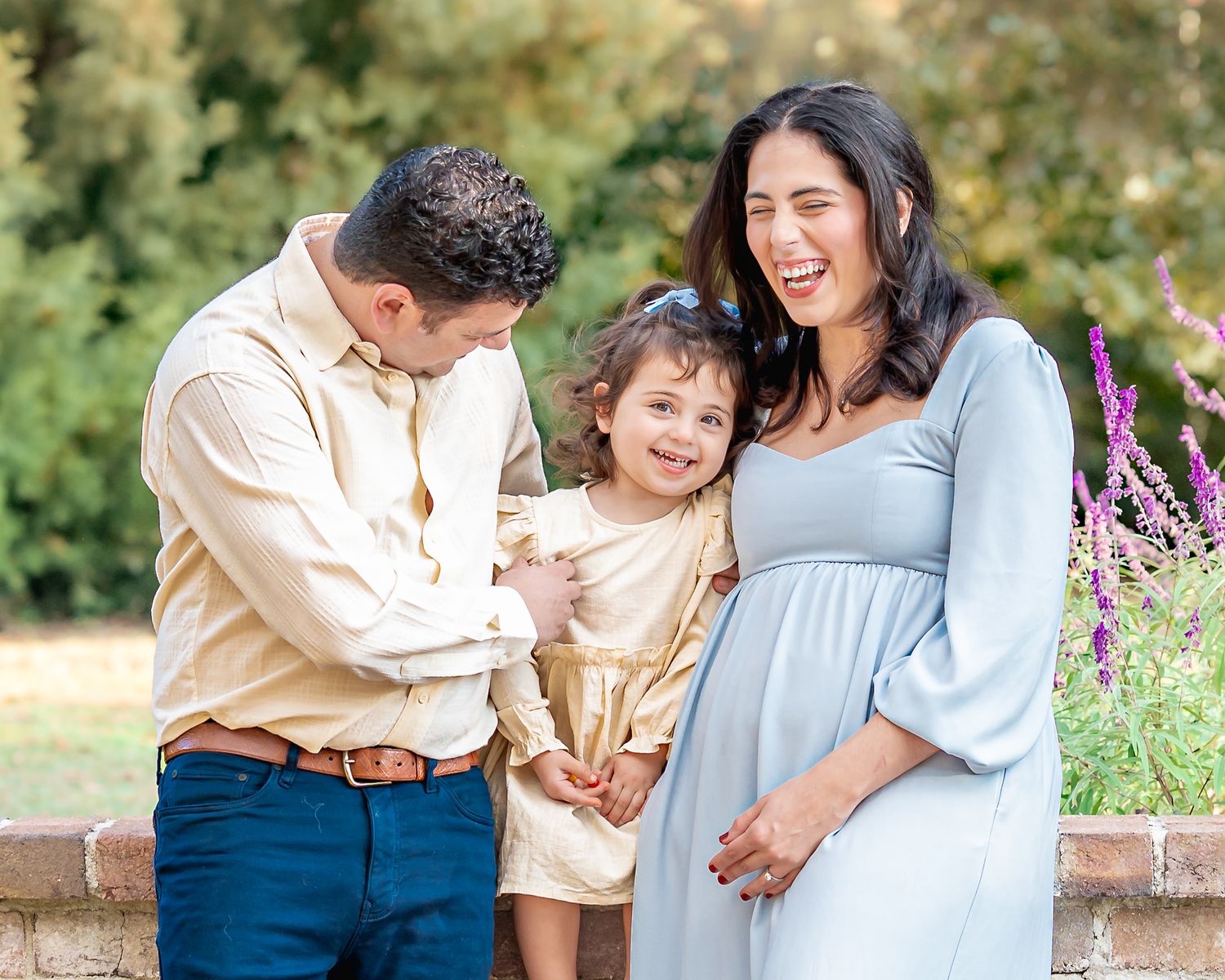 Family maternity photoshoot in a garden with purple flowers at sunset.