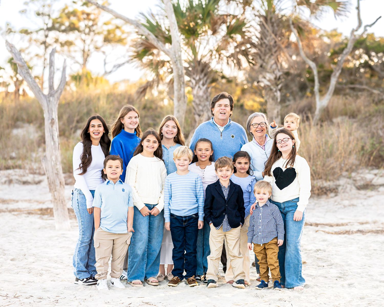Large family group wearing coordinated blue and white outfits posed on beach.