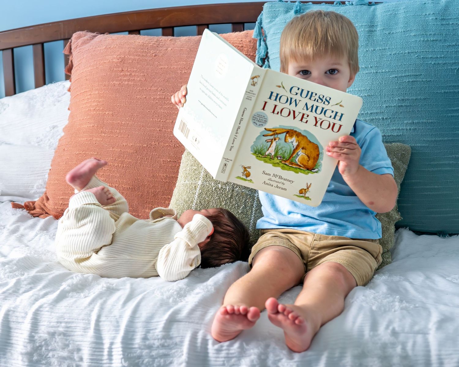 Baby lying on blue bedding while reading a children's picture book.