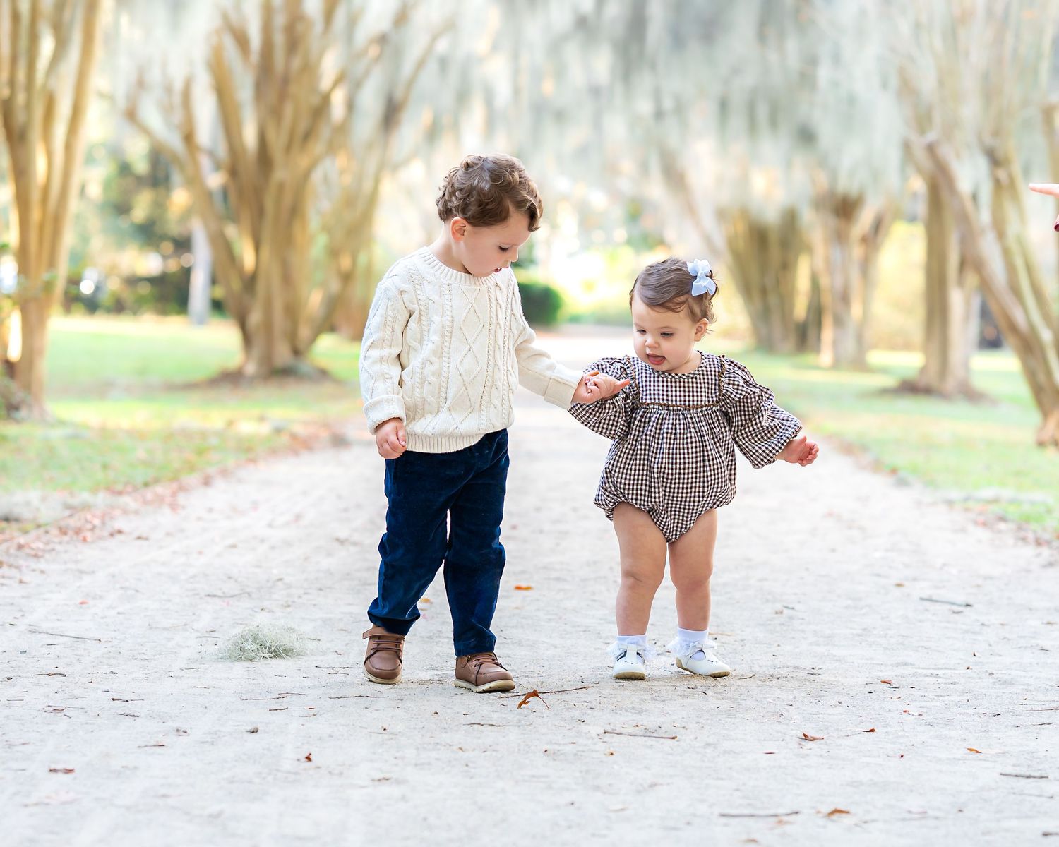 Small children play and crawl on a sandy path during a casual outdoor photoshoot.