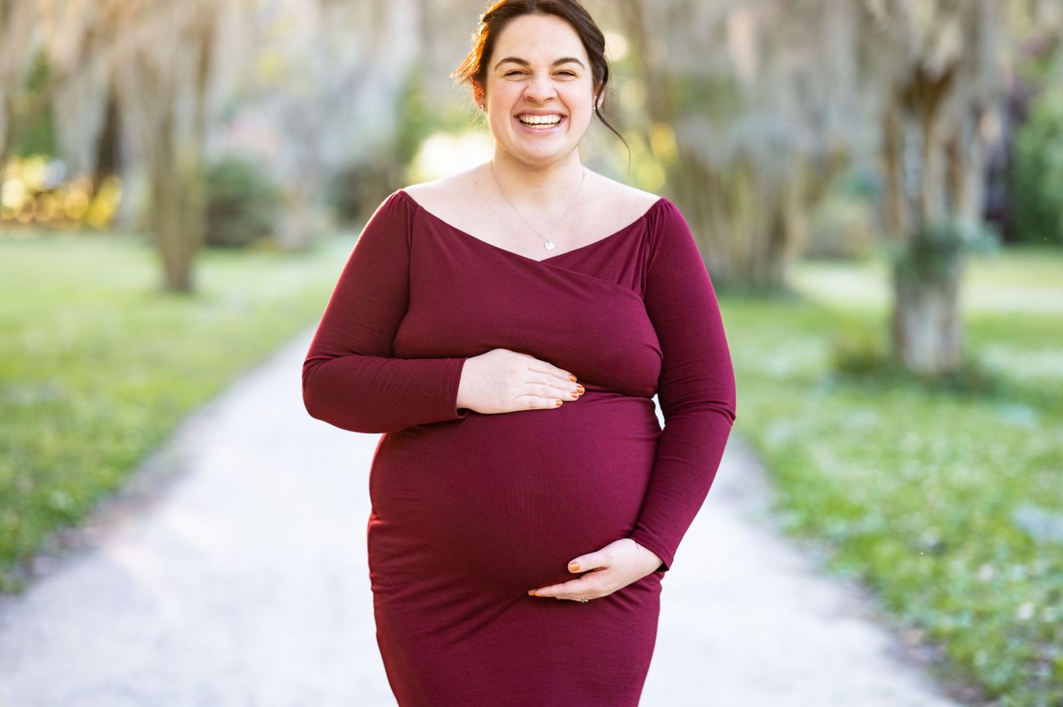 A maternity photoshoot in a burgundy dress outdoors.