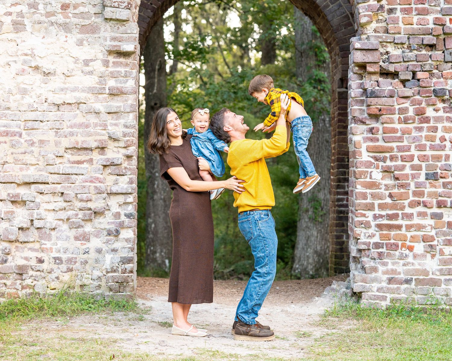 Playful family poses through brick archway during outdoor photo session.